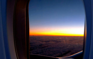 Sunset light shining through an airplane window, with clouds and the horizon visible below.